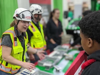 A volunteer in safety vest and hard hat speaks with a middle school student about careers.